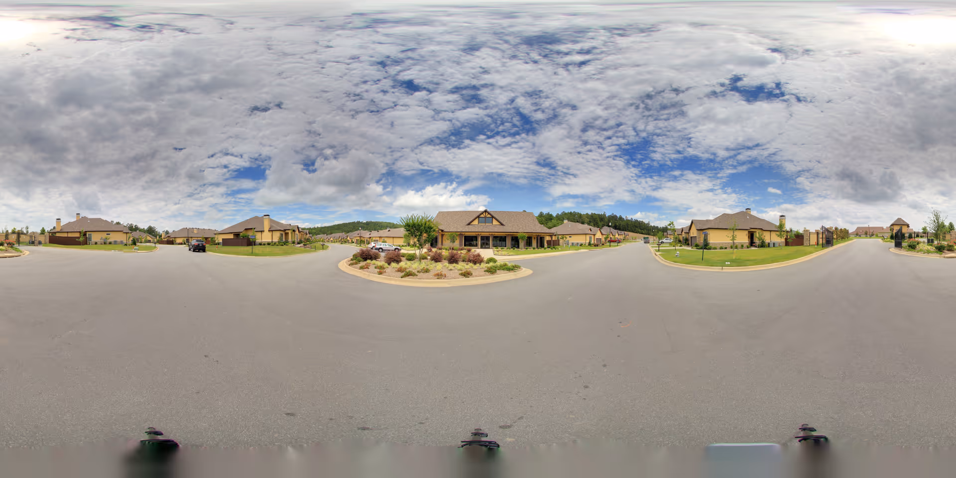 Panoramic exterior view of a neighborhood of single-story cottages and landscaped roundabout under a partly cloudy sky.
