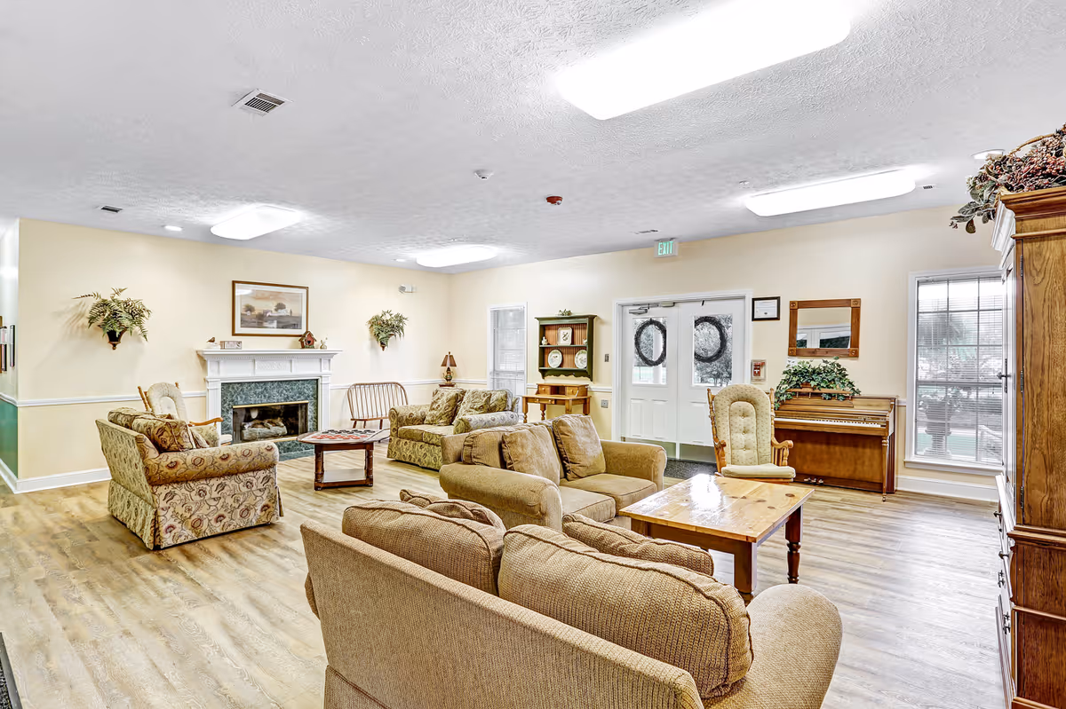 Well-lit common living room with sofas, armchairs, a fireplace, piano, and front doors.