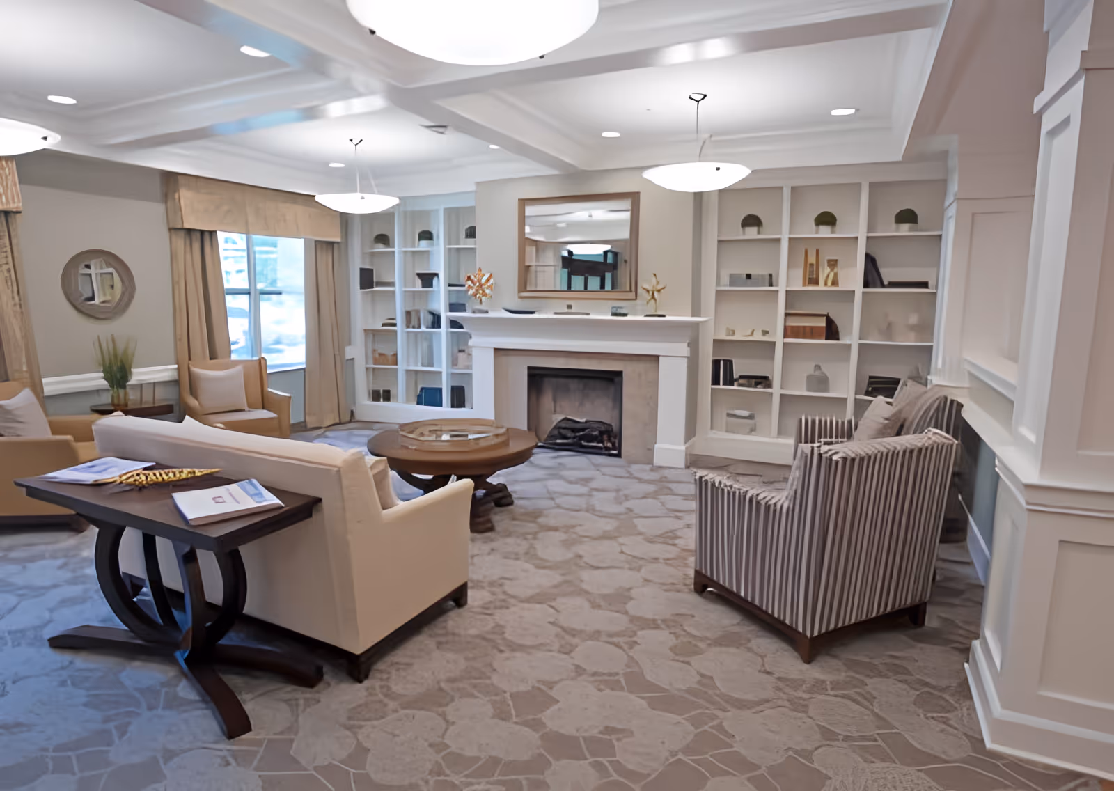 Well-lit senior living lounge with sofas and armchairs arranged around a fireplace and built-in shelving.