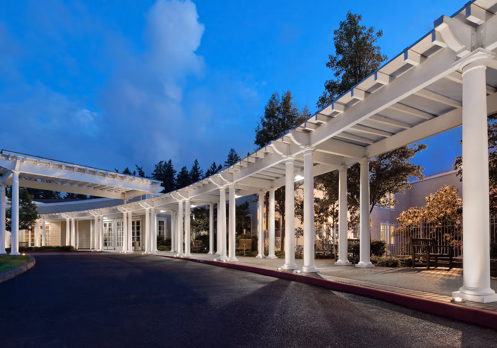 White-columned entrance and walkway frame the exterior of a senior living facility.