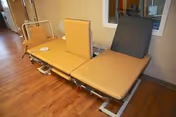 Three tan vinyl medical recliner/exam chairs with adjustable backrests in a room with wood-look flooring and a small window to another area.