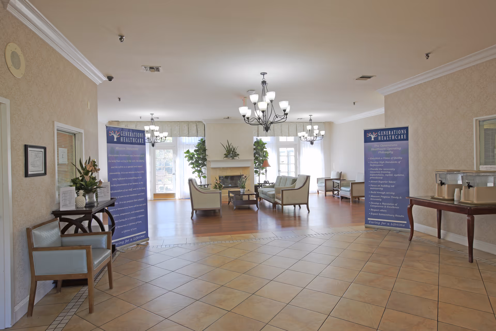 Spacious senior living facility lobby with seating area, chandeliers, fireplace, and informational banners.