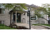 Stone-faced senior living facility entrance with steps, greenery, and a streetlamp.