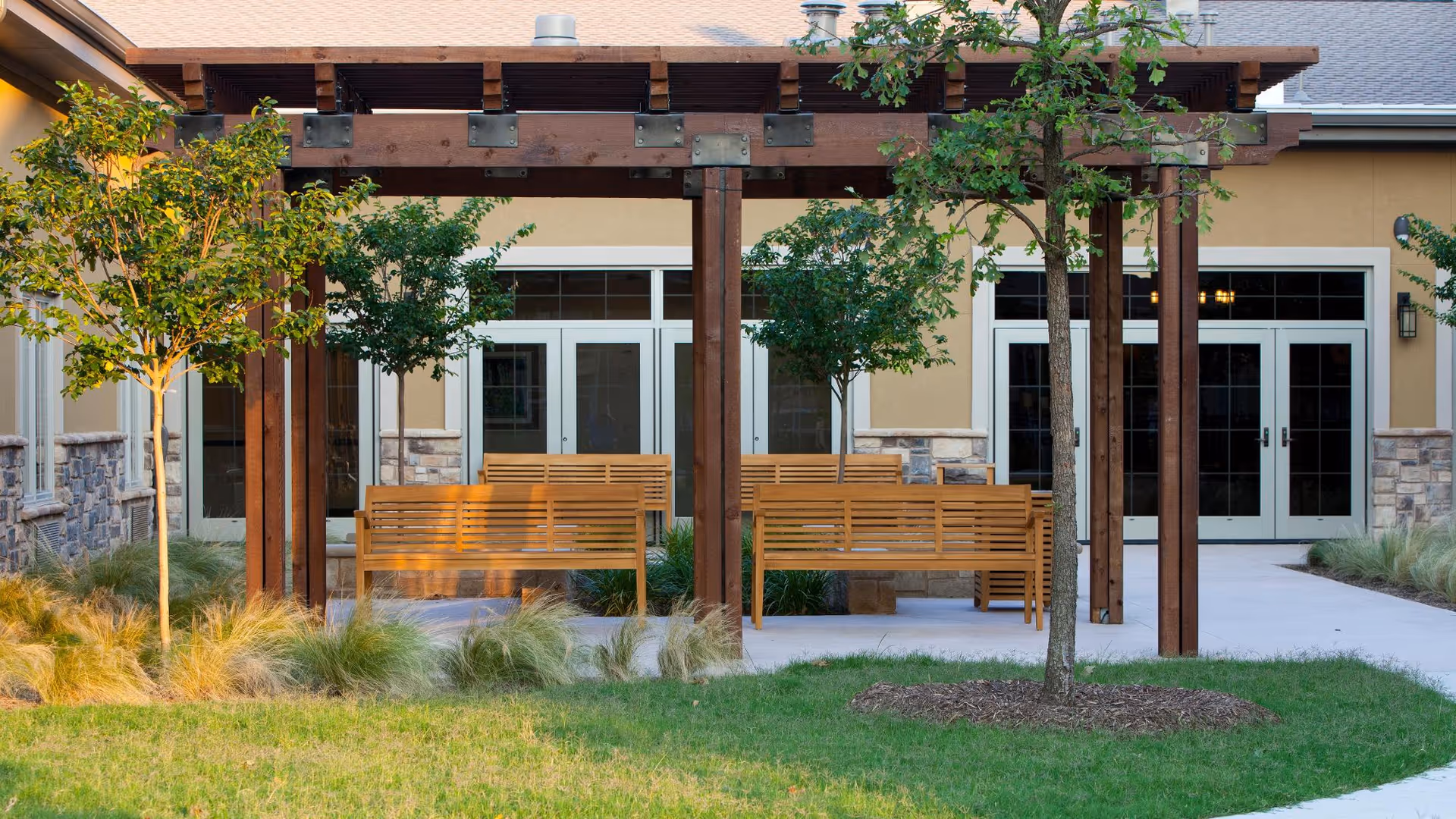 Outdoor courtyard with a wooden pergola and benches in front of a building entrance.