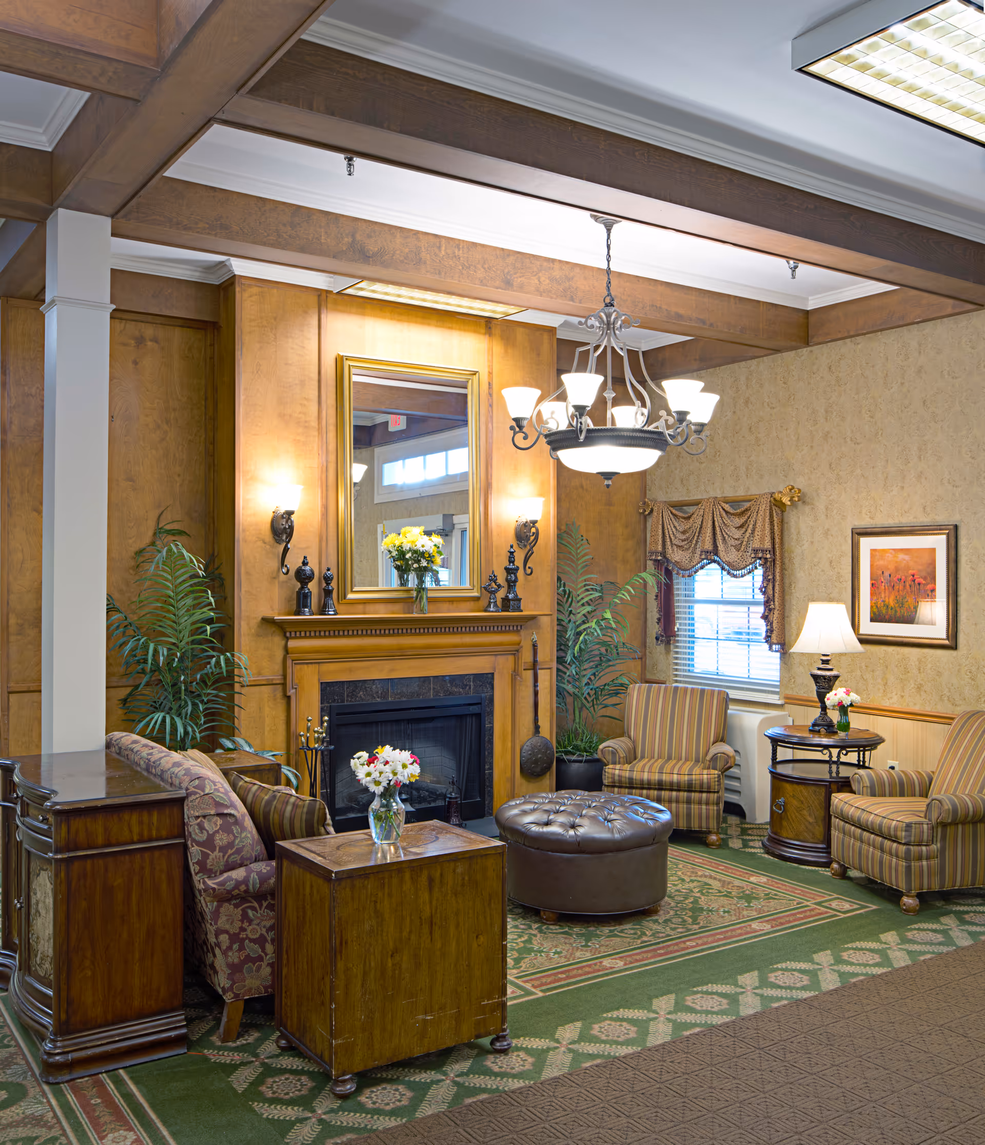 Comfortable living-room style common area with a fireplace, upholstered chairs, ottoman, chandelier, and decorative furnishings.