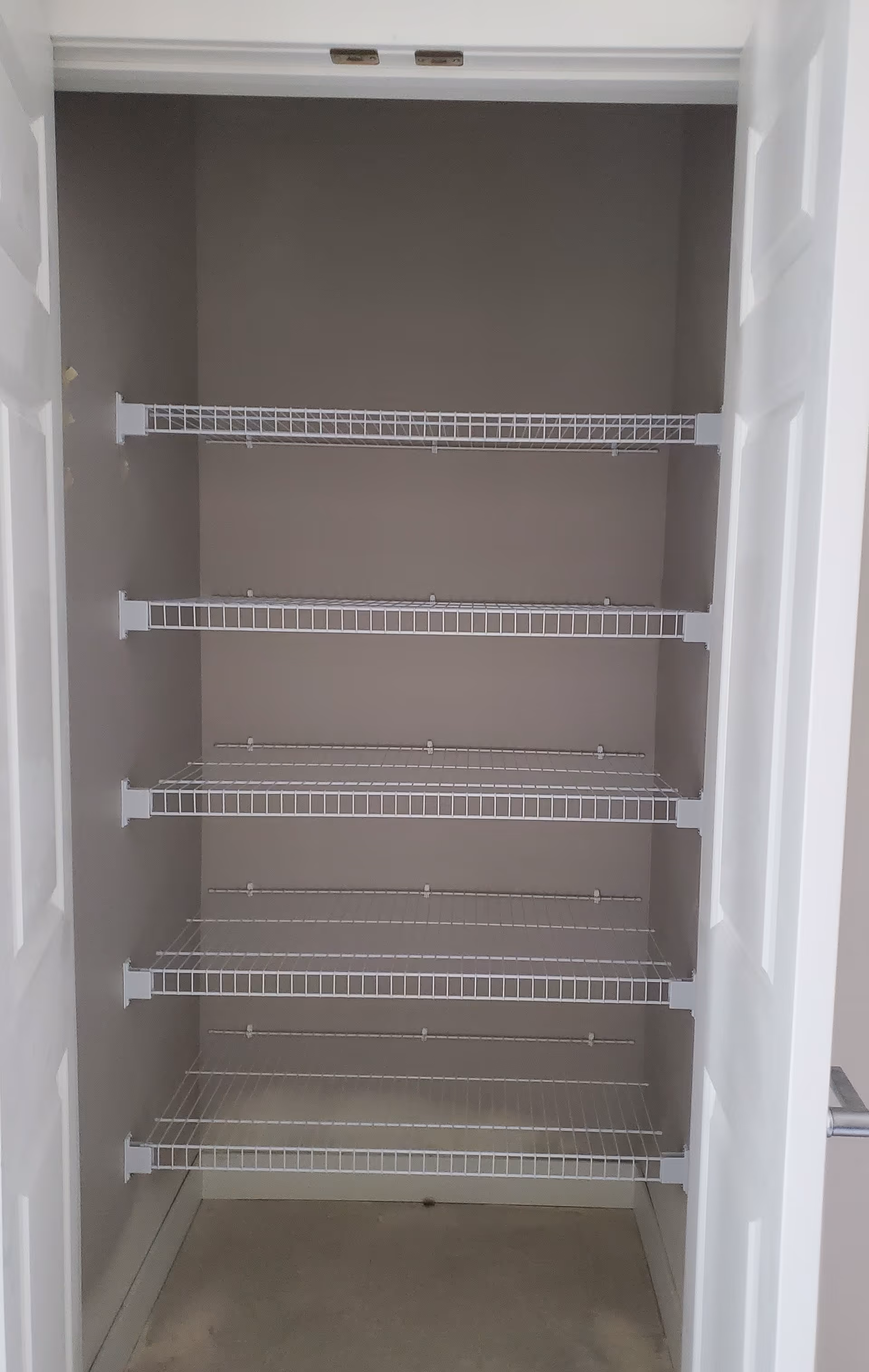 Empty closet or pantry with five white wire shelves mounted on the walls, with white double doors open to reveal the interior.