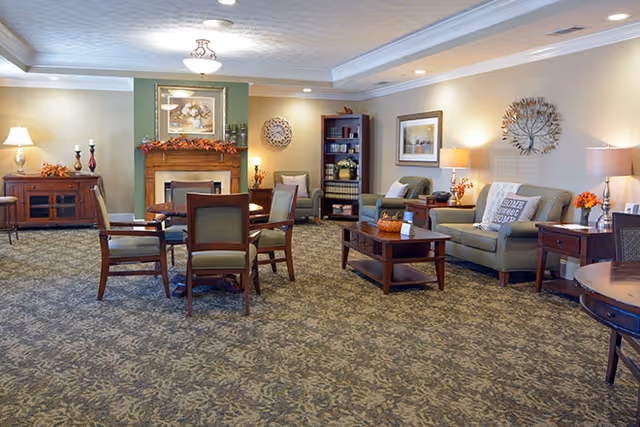 Spacious senior living community lounge with sofas, armchairs, coffee tables, a fireplace, and warm lamps.