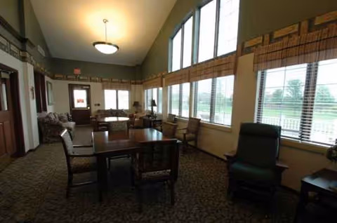 Spacious senior living common area with a long table, chairs, and large windows.