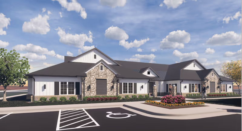 Front view of a single-story senior care building with stone and white siding facade, landscaped entrance and a handicap parking space.