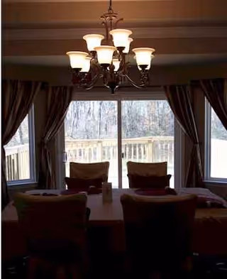 Dimly lit dining area with a chandelier and large windows behind draped curtains.