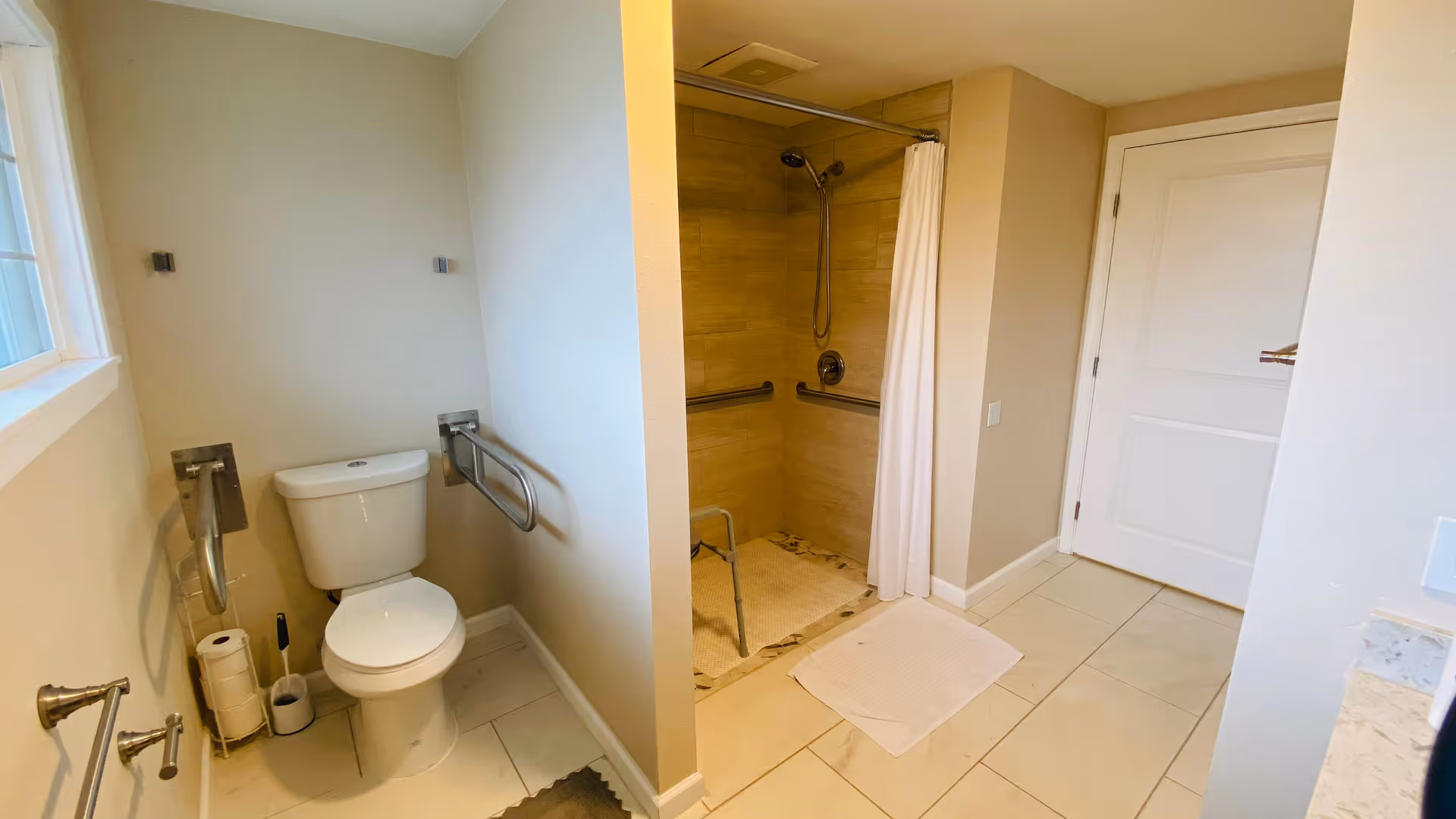 Accessible bathroom with a toilet, wall-mounted grab bars, and a walk-in shower with a curtain.