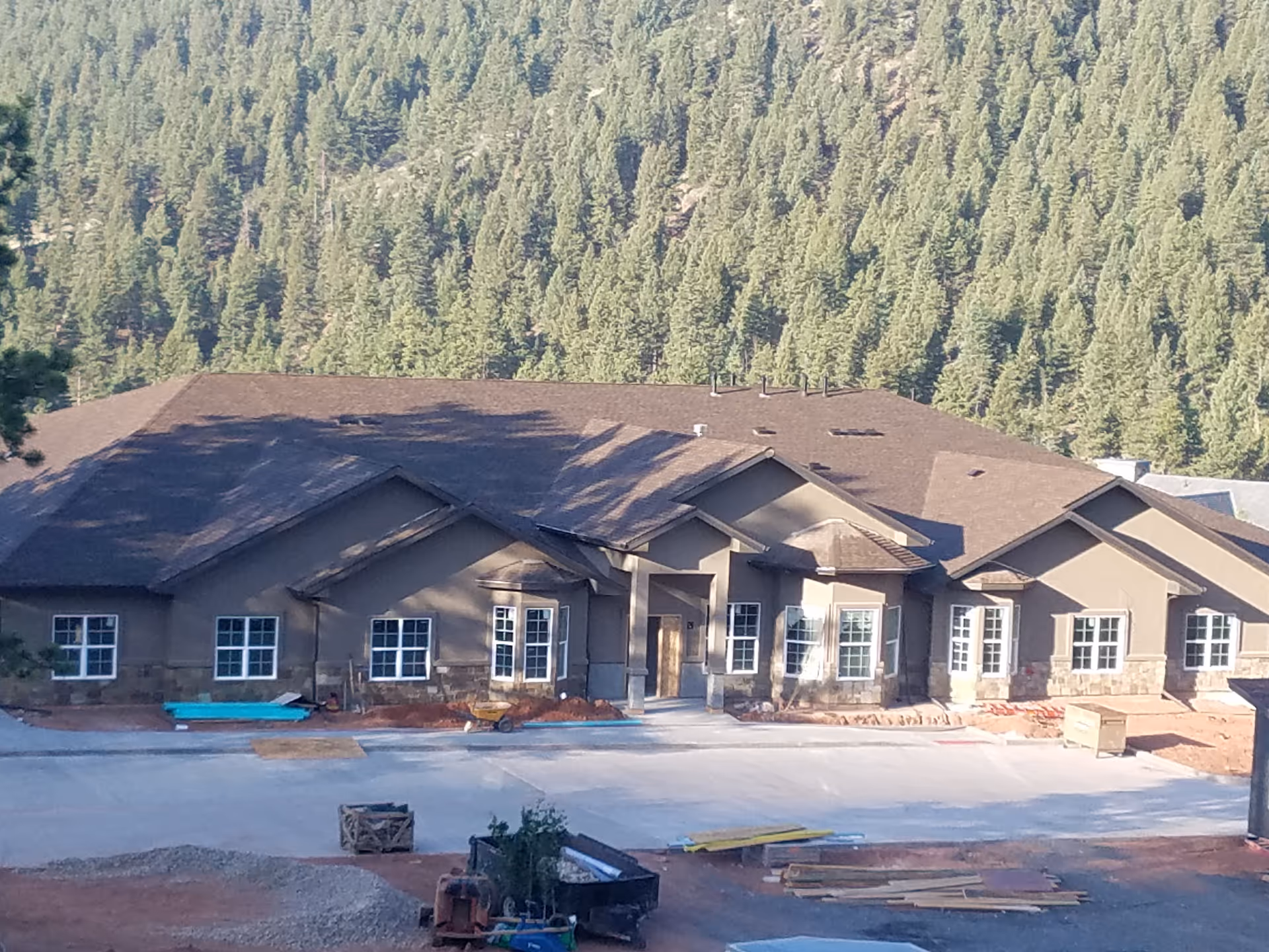 Front view of a single-story senior living building under construction with a large forested hillside behind it.