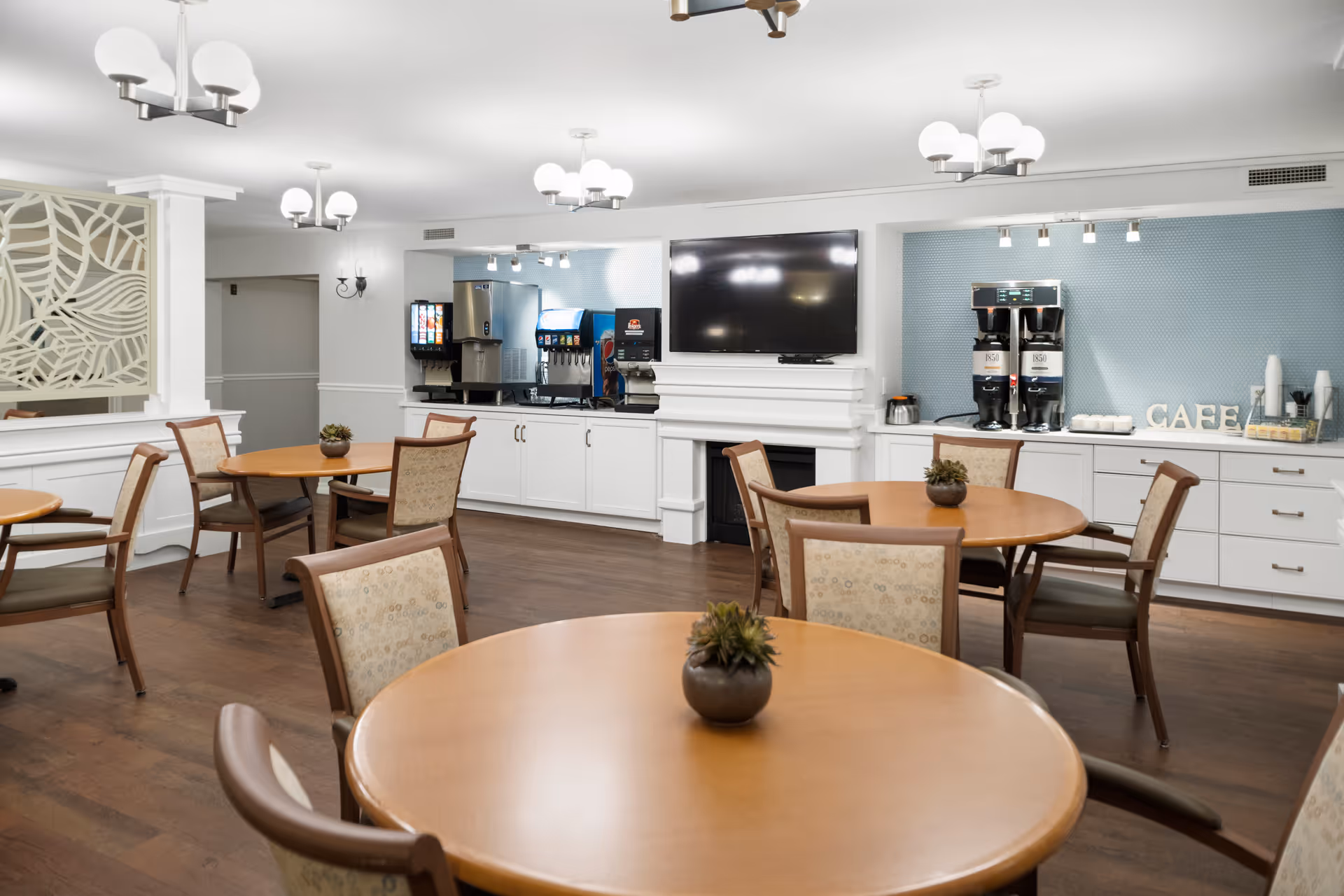 A cozy dining area with round tables and a coffee station in a senior living facility.
