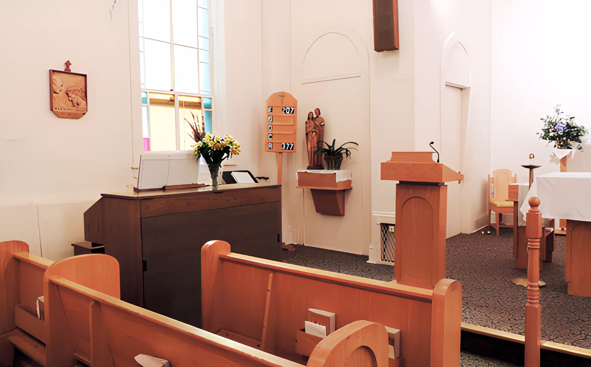 Small chapel interior with wooden pews, a pulpit, altar, organ, and stained glass window.