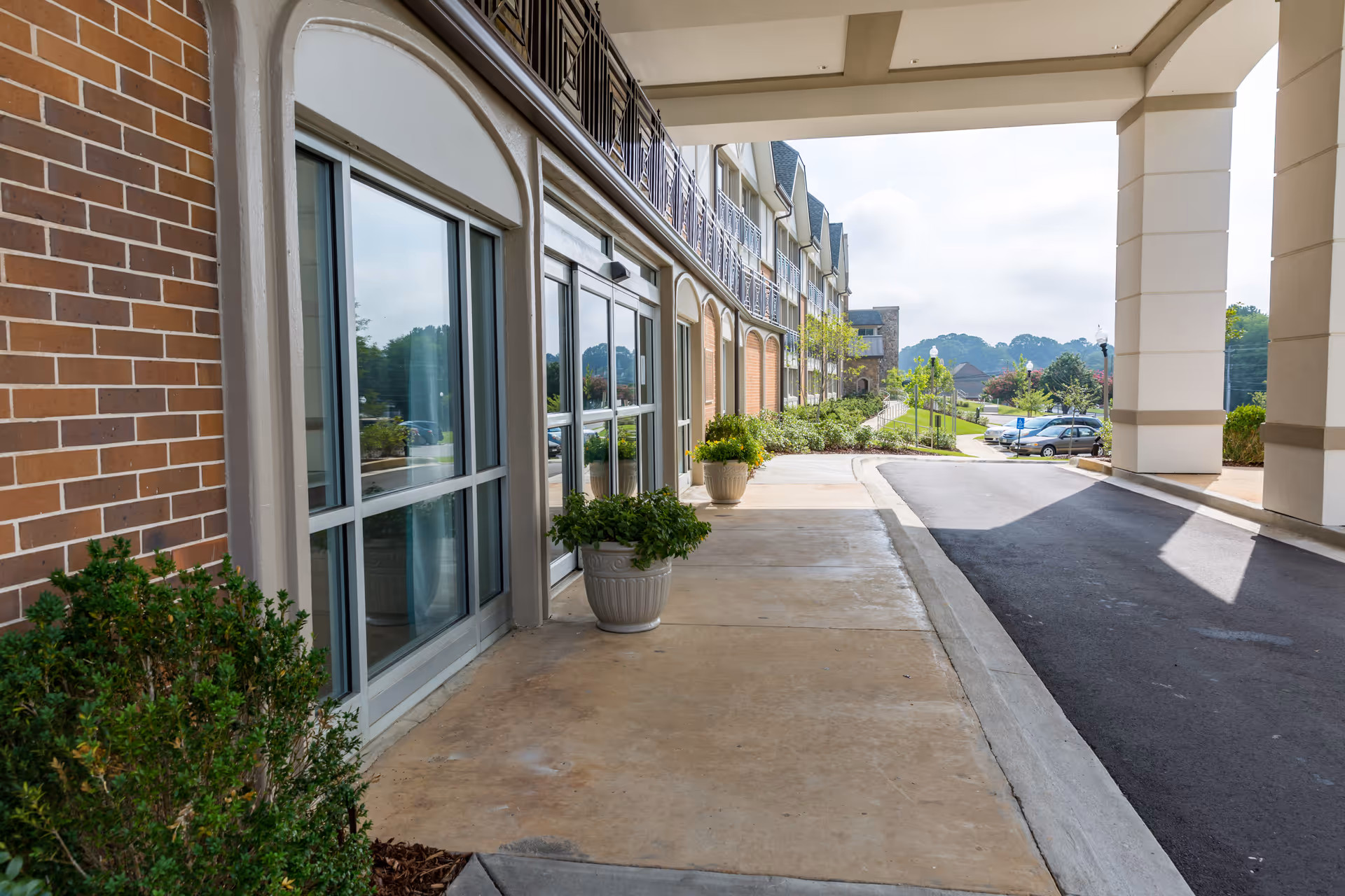 Covered entrance drive and sidewalk beside a multi-story senior living building with planters and large windows.