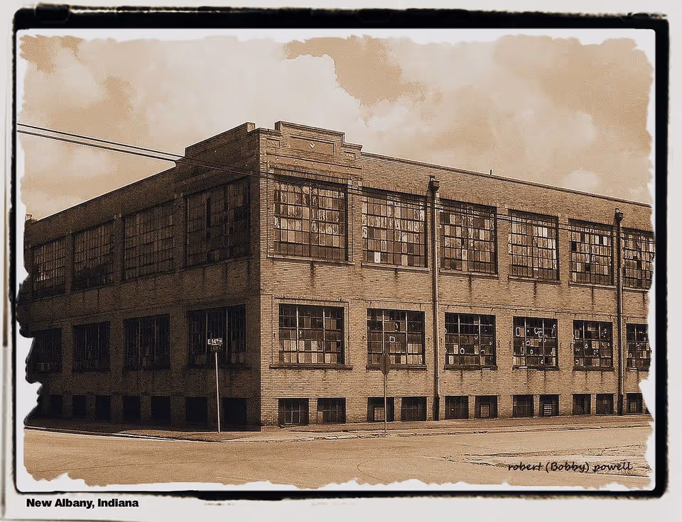 Sepia-toned photograph of an old industrial brick building with many large, multi-pane windows, located at a street corner in New Albany, Indiana. The building appears weathered and aged, with some windows broken or boarded up. The sky is partly cloudy.