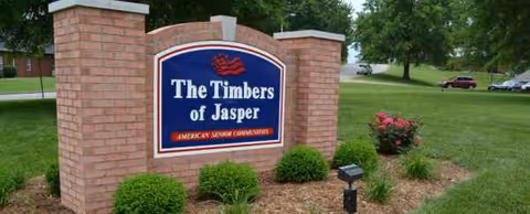 Brick entrance sign for The Timbers of Jasper with shrubs and manicured landscaping
