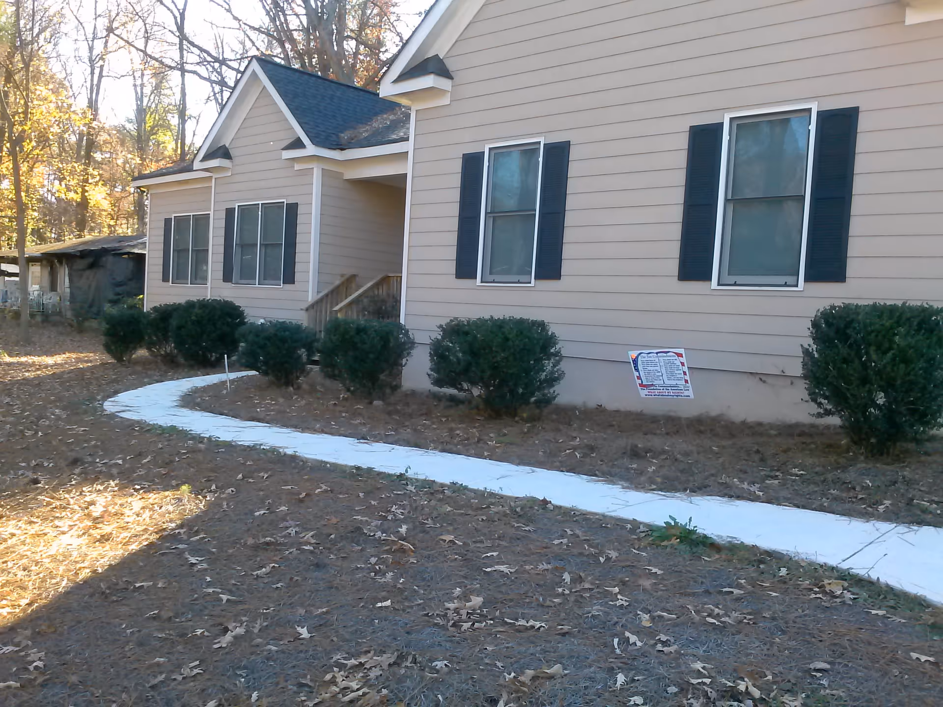Front exterior of a beige single-story house with a curved white walkway and shrubs.