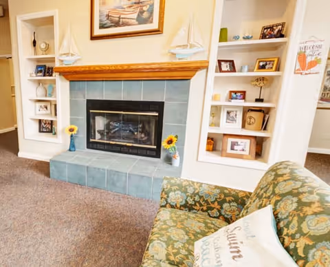 Cozy seating area with a tiled fireplace flanked by built-in shelves and a patterned armchair in the foreground.