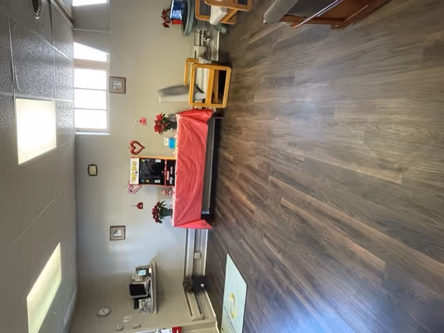 Cozy common lounge with a red tablecloth-covered table, chairs, plants, and wall decor.