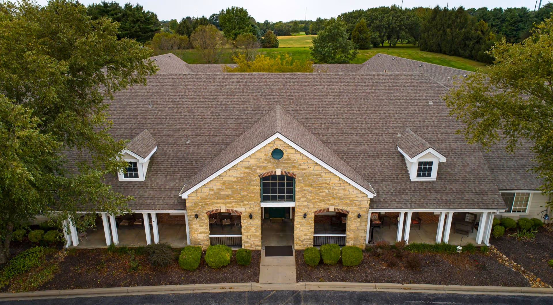 Aerial front view of a single-story assisted living building with a stone entrance, covered porch and surrounding landscaping.