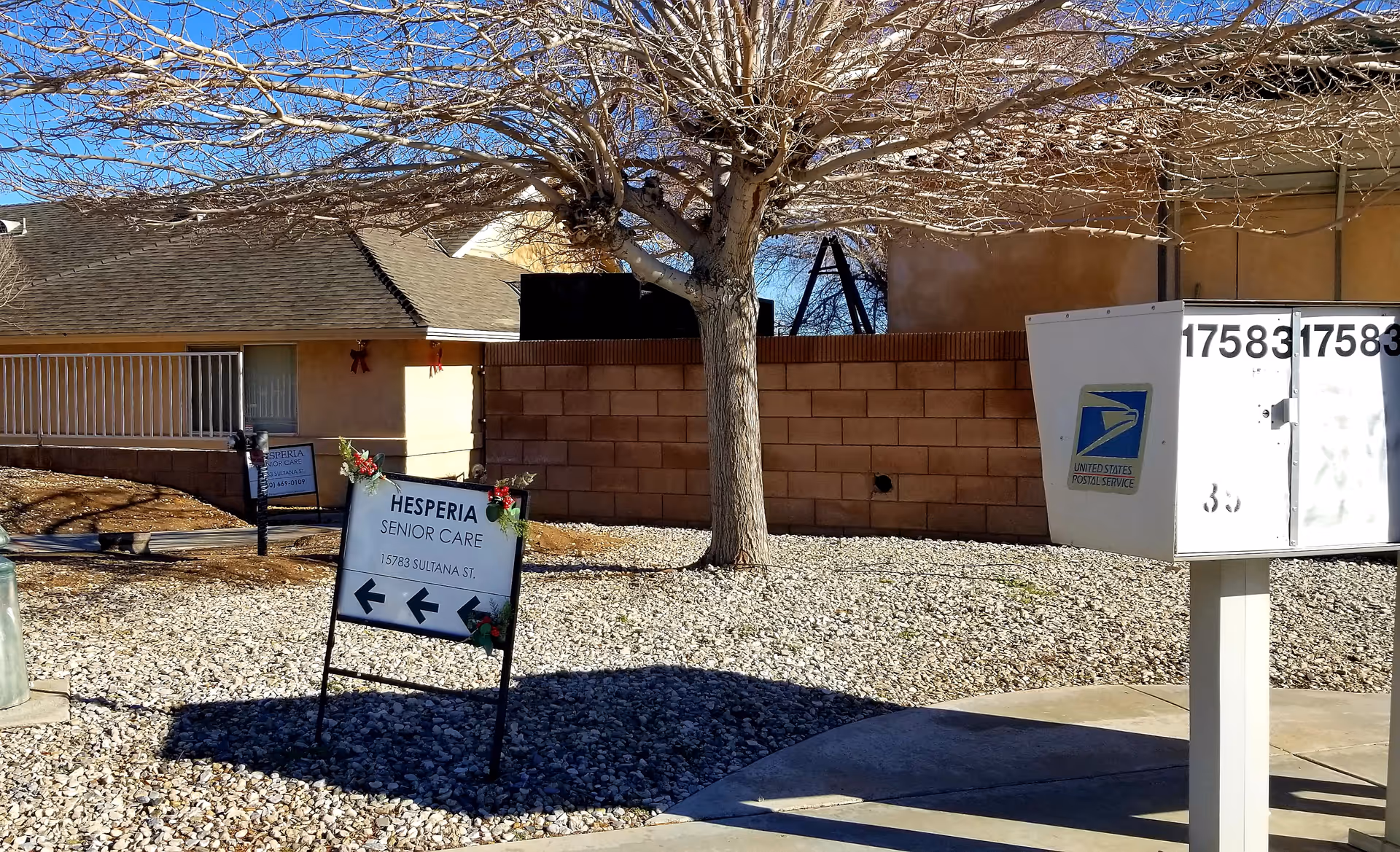 Front exterior of Hesperia Senior Care with a sign, a tree, and a gravel yard.