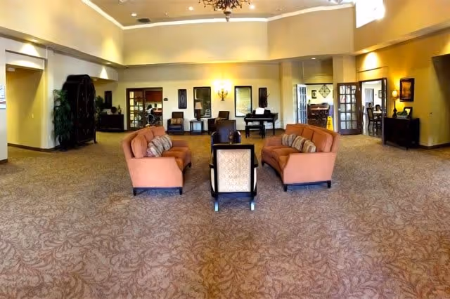 Spacious seating area and lobby with two sofas, chairs, a piano and warm lighting in a common room.