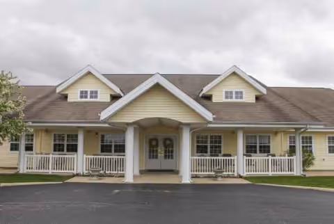 Front view of a beige senior living facility with a covered entry and white railings.