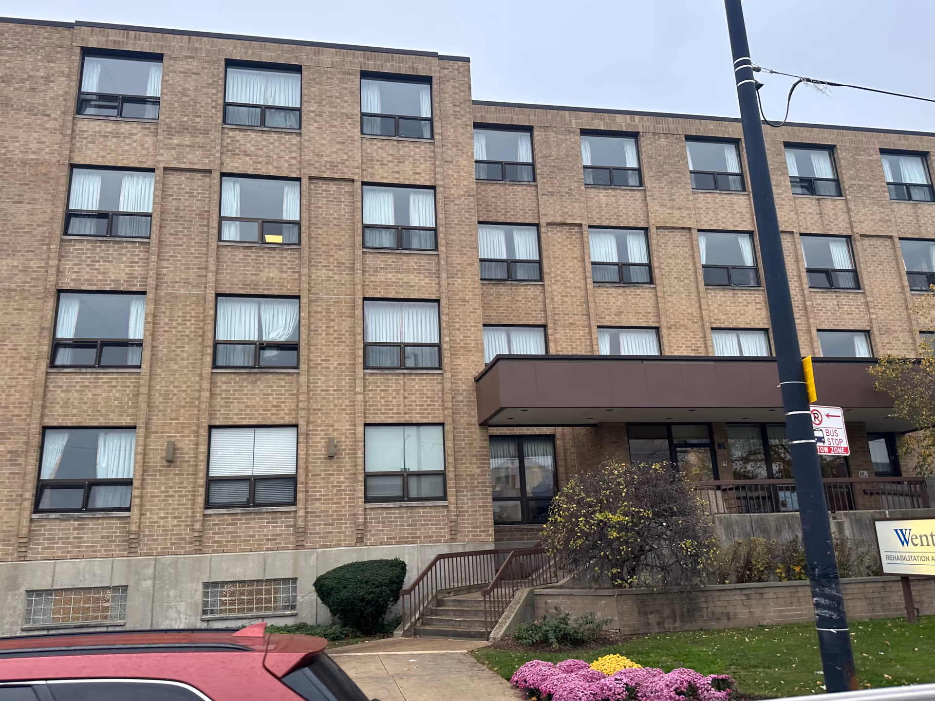 Front exterior of a brick multi-story rehab and health care center with an entrance canopy, steps, windows, and a flowerbed.