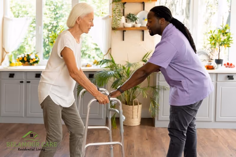 An elderly woman using a walker is being supported by a caregiver in a bright kitchen area.