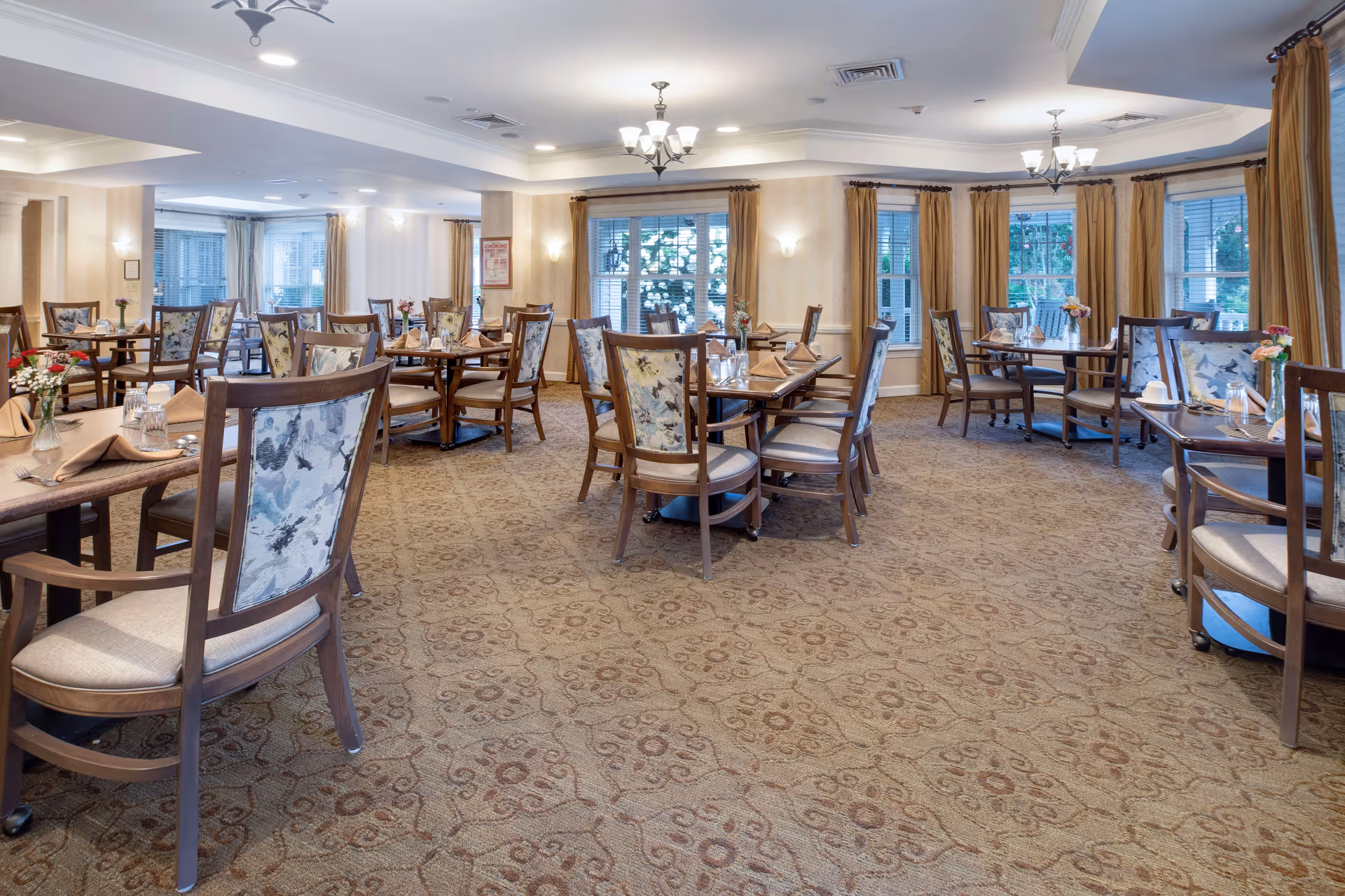 Spacious, well-lit dining room with multiple tables and upholstered chairs set for meals.
