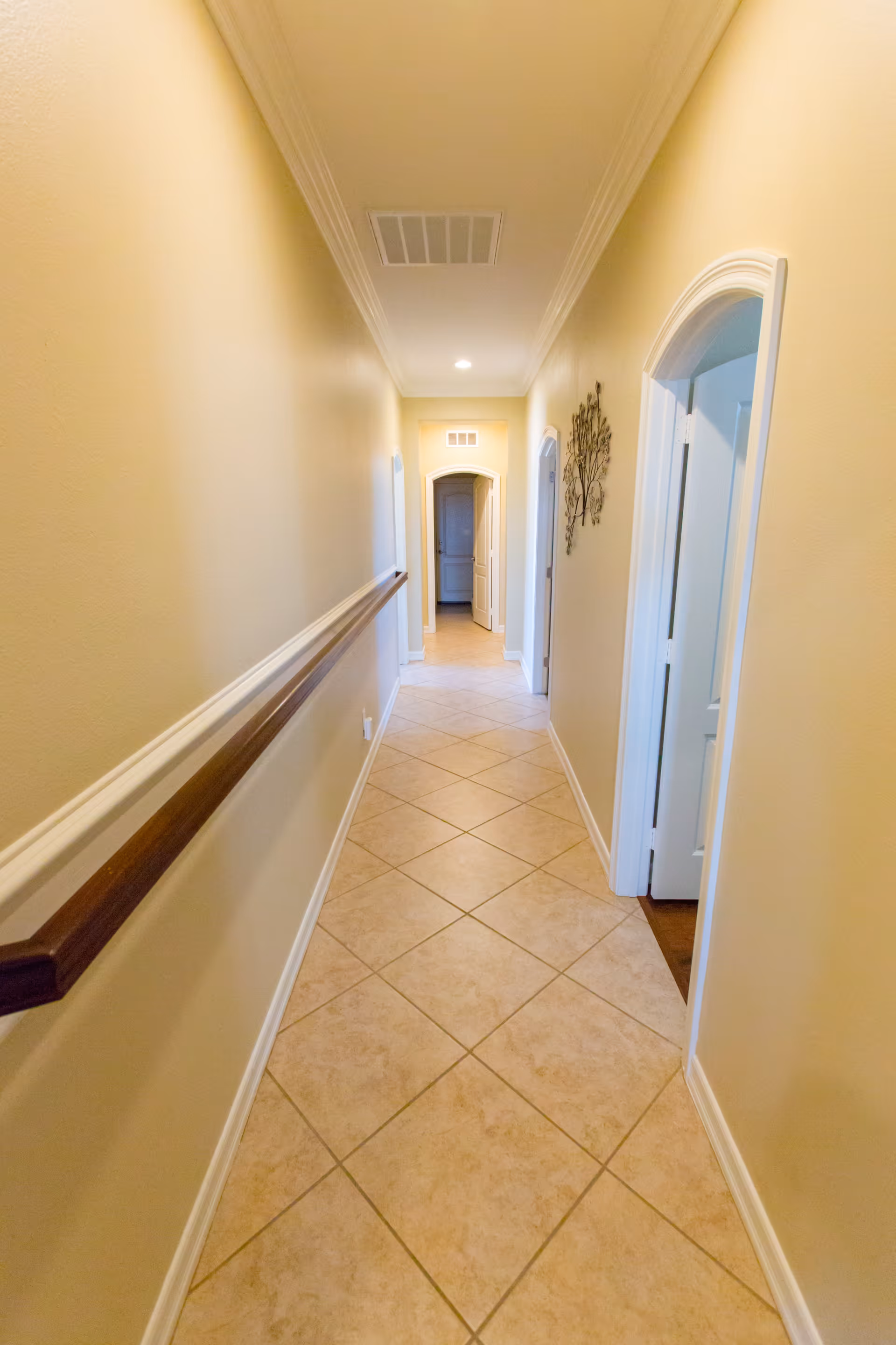 Long tiled interior hallway with a wooden handrail and doors along the sides leading to an arched doorway.