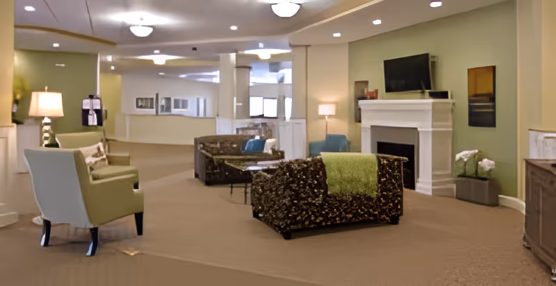Spacious senior living lounge with armchairs, sofas, a fireplace, and a wall-mounted TV.