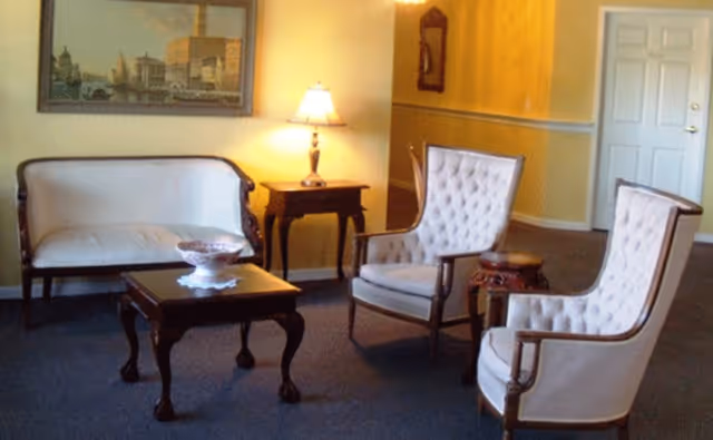 Carpeted sitting area with a loveseat, two upholstered armchairs, a coffee table and a side table with a lamp.