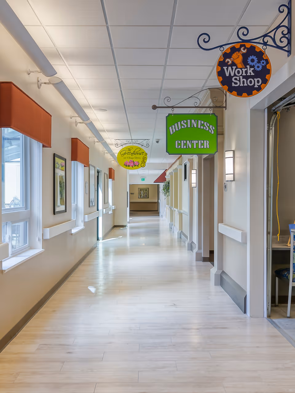 Sunlit interior corridor with hanging 'Business Center' and 'Work Shop' signs and windows along one side.