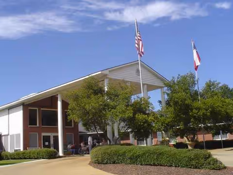 Front exterior of Colonial Pines Healthcare Center with flags, trees, and a shaded entrance.