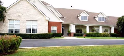 Single story senior living facility exterior with brick facade, front entrance, and manicured lawn.