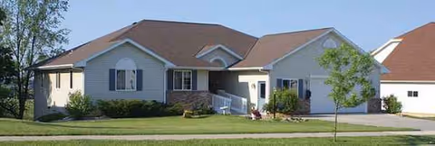 Front exterior of a single-story senior living facility with a manicured lawn and driveway.
