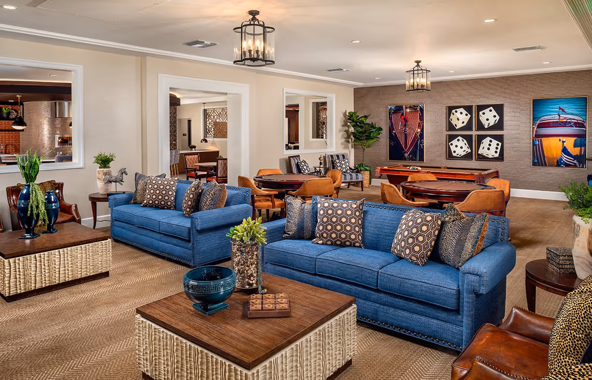 Spacious furnished common lounge with blue sofas, coffee tables, game tables, and wall artwork.