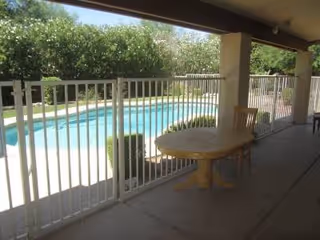 Covered patio overlooking a rectangular pool with white railing and round pedestal table