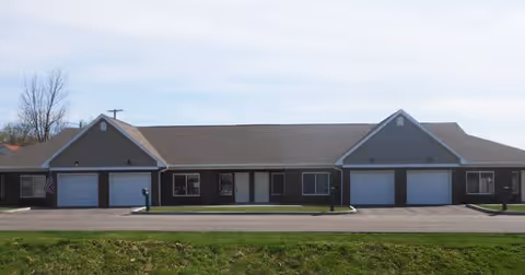 Single-story residential building with multiple attached garages and a front lawn under a blue sky.