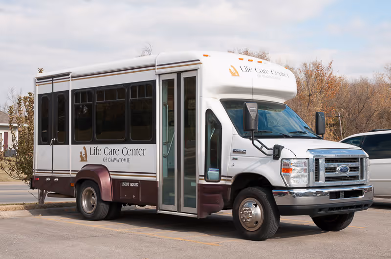 A white and maroon Life Care Center shuttle bus parked in a lot.