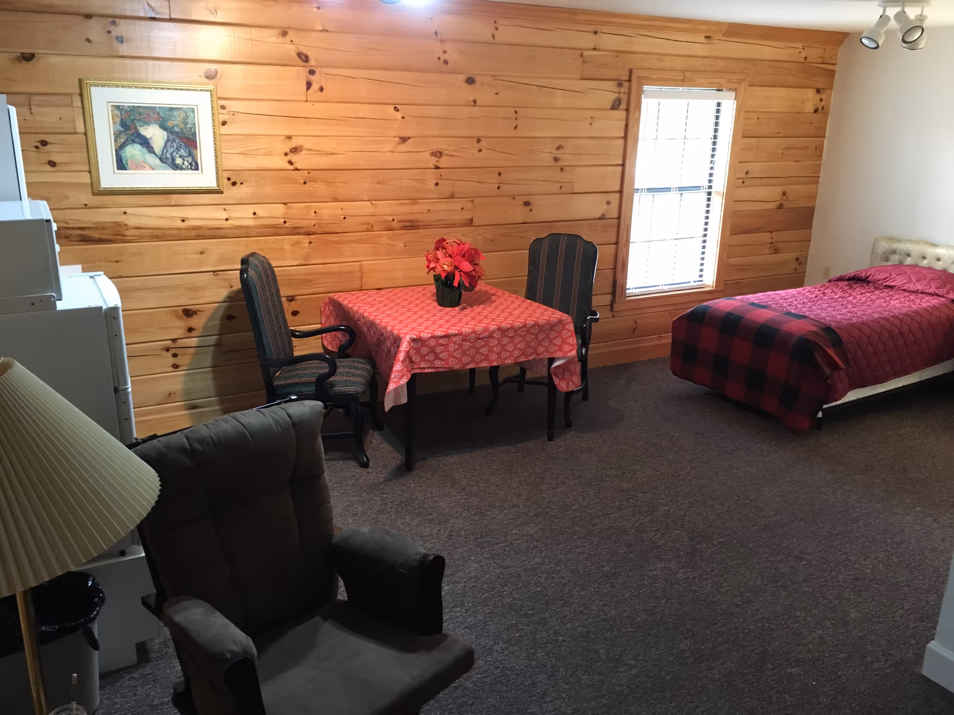 A wood-paneled room with a single bed, a small table with chairs, and a recliner armchair.