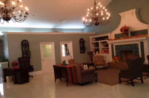 A spacious senior living lounge with sofas, chairs, a fireplace, and chandeliers.