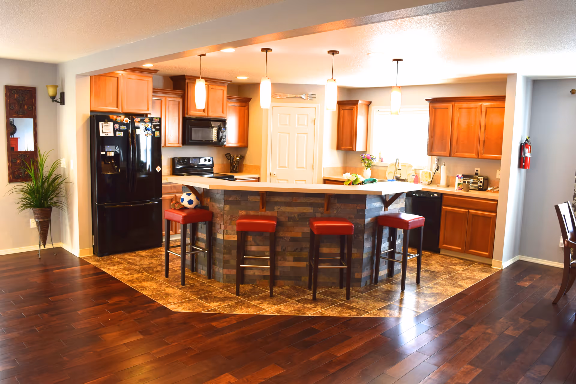 Open modern kitchen with a central island surrounded by red stools, wooden cabinets, and black appliances.