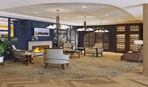 Comfortable communal lounge with upholstered chairs, small tables, a fireplace, chandeliers, and a wine display.