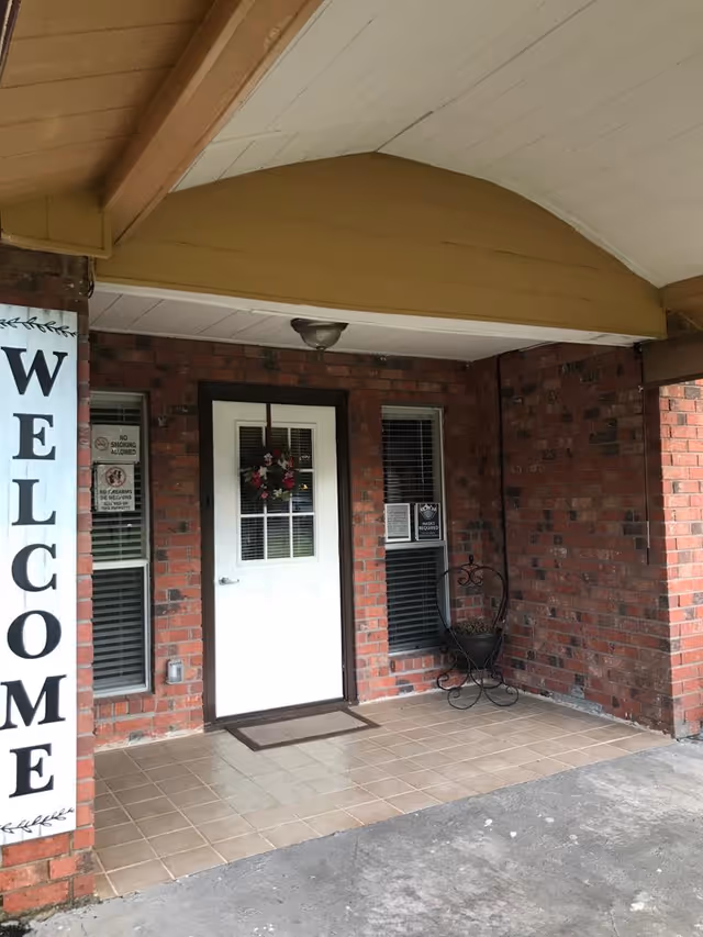 Covered brick entryway with a white door, welcome sign, and a tiled porch.