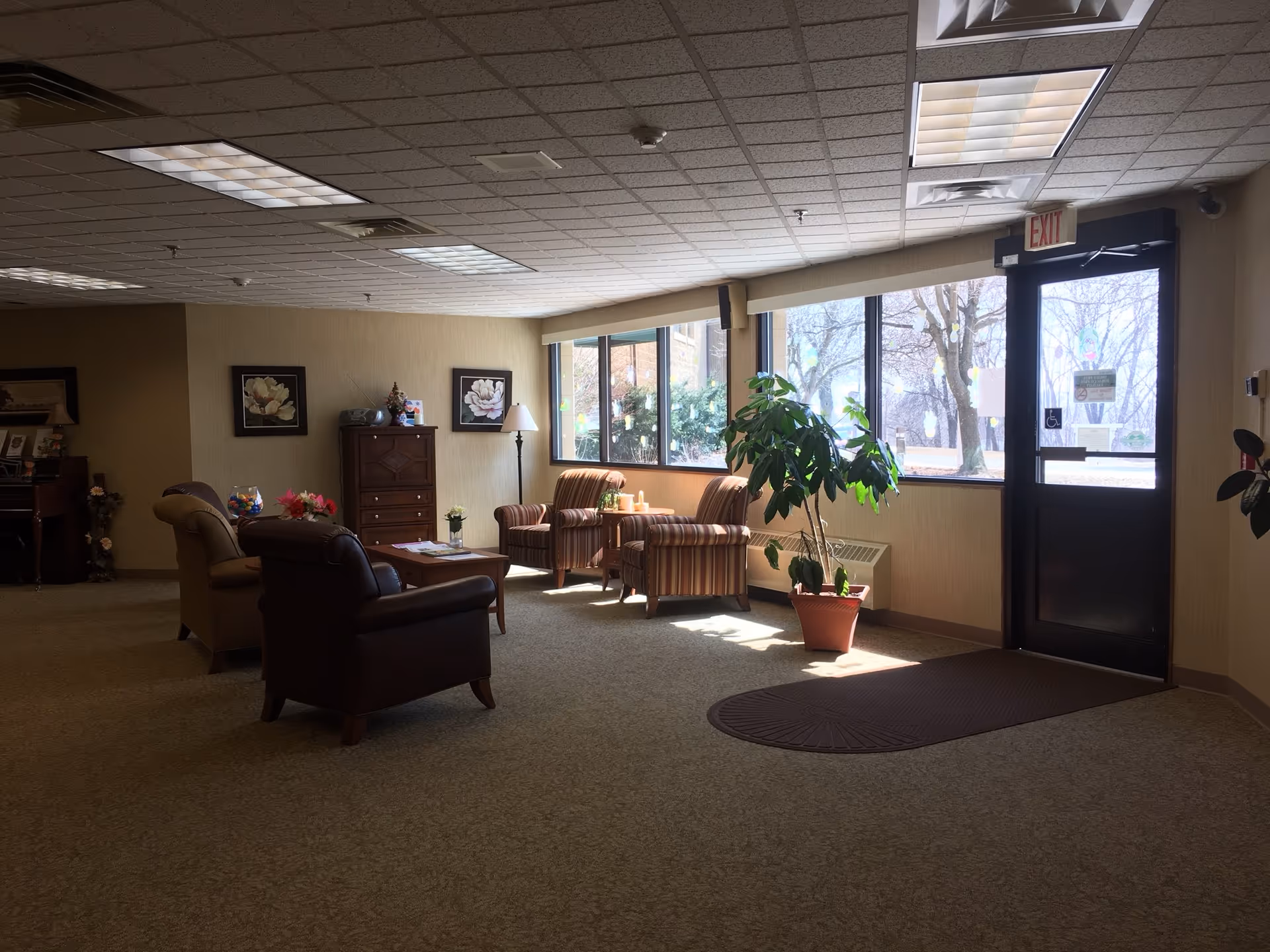 Lobby-style seating area with armchairs, a plant, and large windows near an exit door.