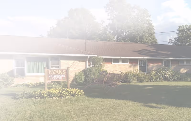 One-story brick retirement center with a lawn, landscaping, a sign reading "Evans Retirement Center" and an old wagon wheel in front.