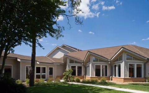 A single-story senior living facility with tan exterior, multiple windows, and manicured landscaping.